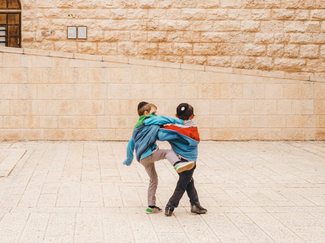 2 boys in green and blue jacket walking on gray concrete floor during daytime