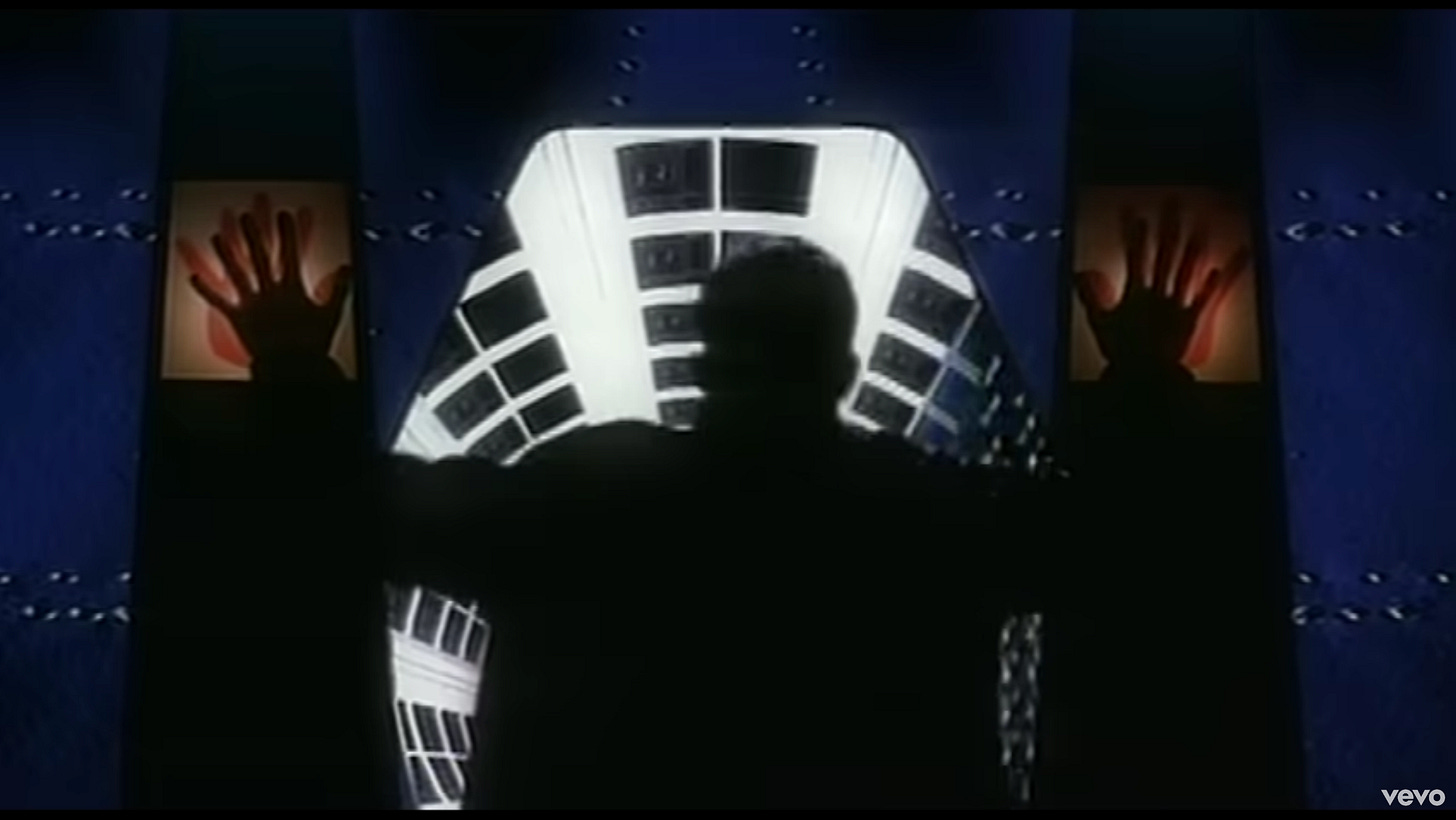 A silhouette stands in front of a space doorway, and there are two red hands on either side. The silhouette has placed his hands on those, and the door is open, and he can see down another space hallway.