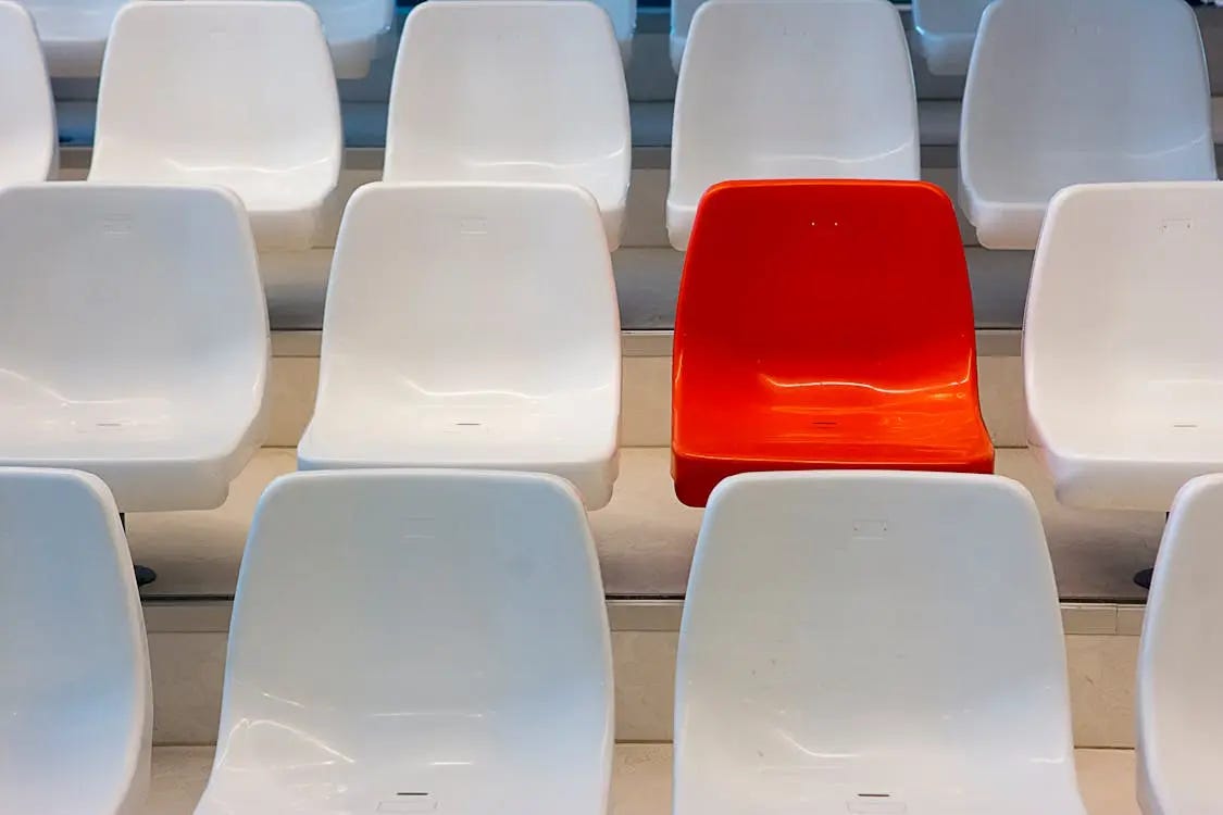 Rows of white seats with one red chair standing out among them that shows isolation that is felt for Mexican Americans who try to assimilate.