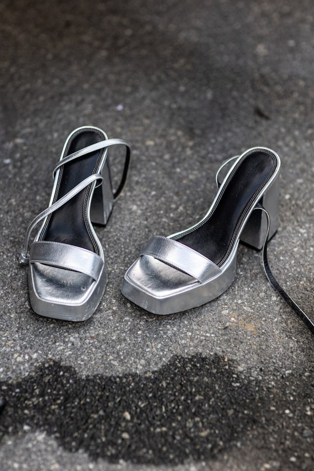 Silver high-heeled shoes on asphalt.