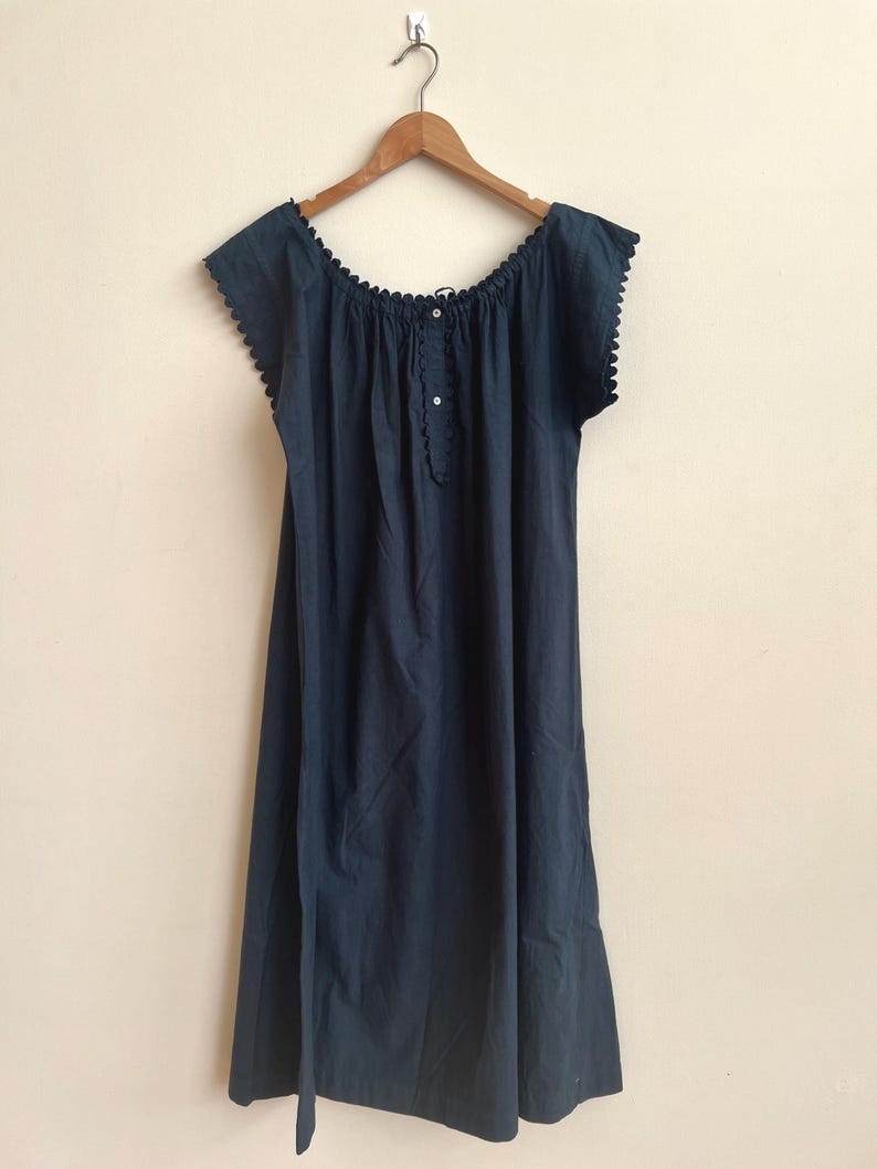 May include: A navy blue dress with a scalloped neckline and short sleeves, hanging on a wooden hanger. The dress features a button-down front and a flowing, knee-length skirt. The fabric appears to be a soft, lightweight material.