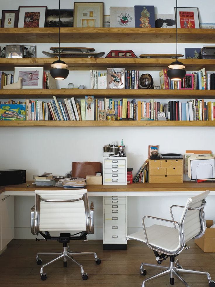 This may contain: two white office chairs sitting in front of a desk with bookshelves above it