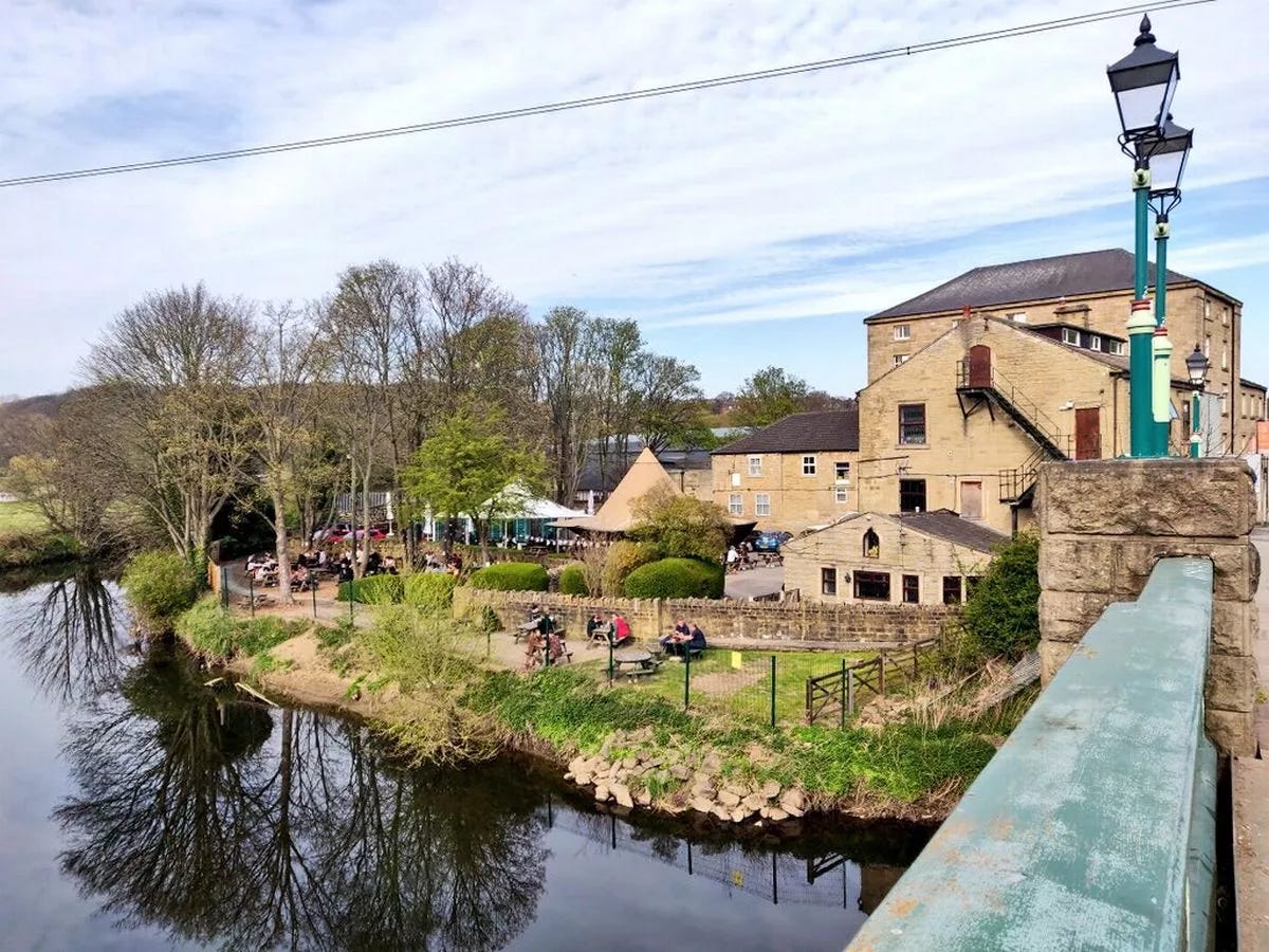 The tavern, set across the bridge with greenery around it and the beer garden by the canal The tavern, set across the bridge with greenery around it and the beer garden by the canal