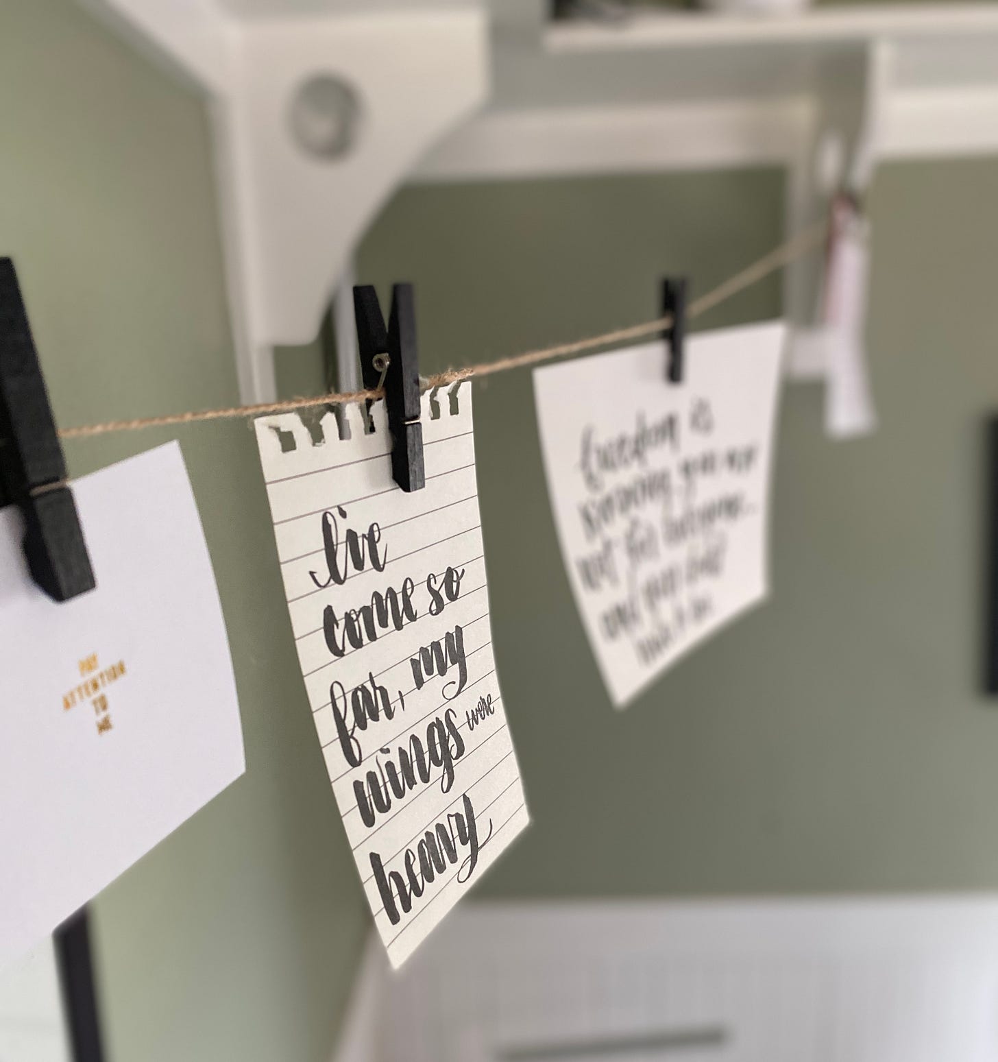 a picture of Rose’s calligraphy hung on a piece of twine with a black clothes pin. The script reads “I’ve come so far, my wings were heavy.” a picture of Rose’s calligraphy hung on a piece of twine with a black clothes pin. The script reads “I’ve come so far, my wings were heavy.”