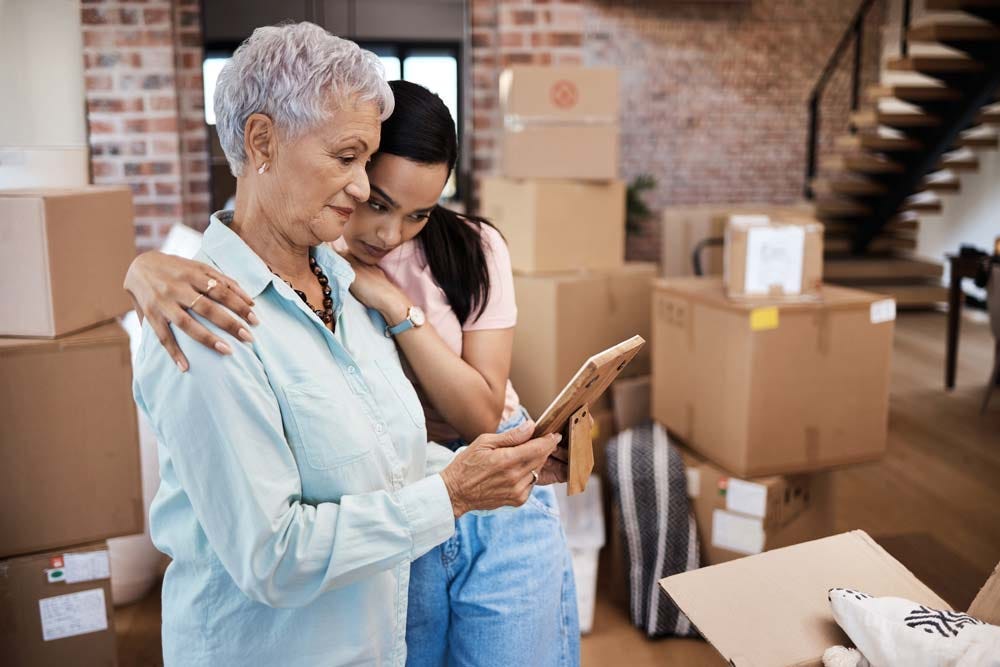 Photo of a senior woman looking at a photograph with her adult daughter while packing boxes on moving day.