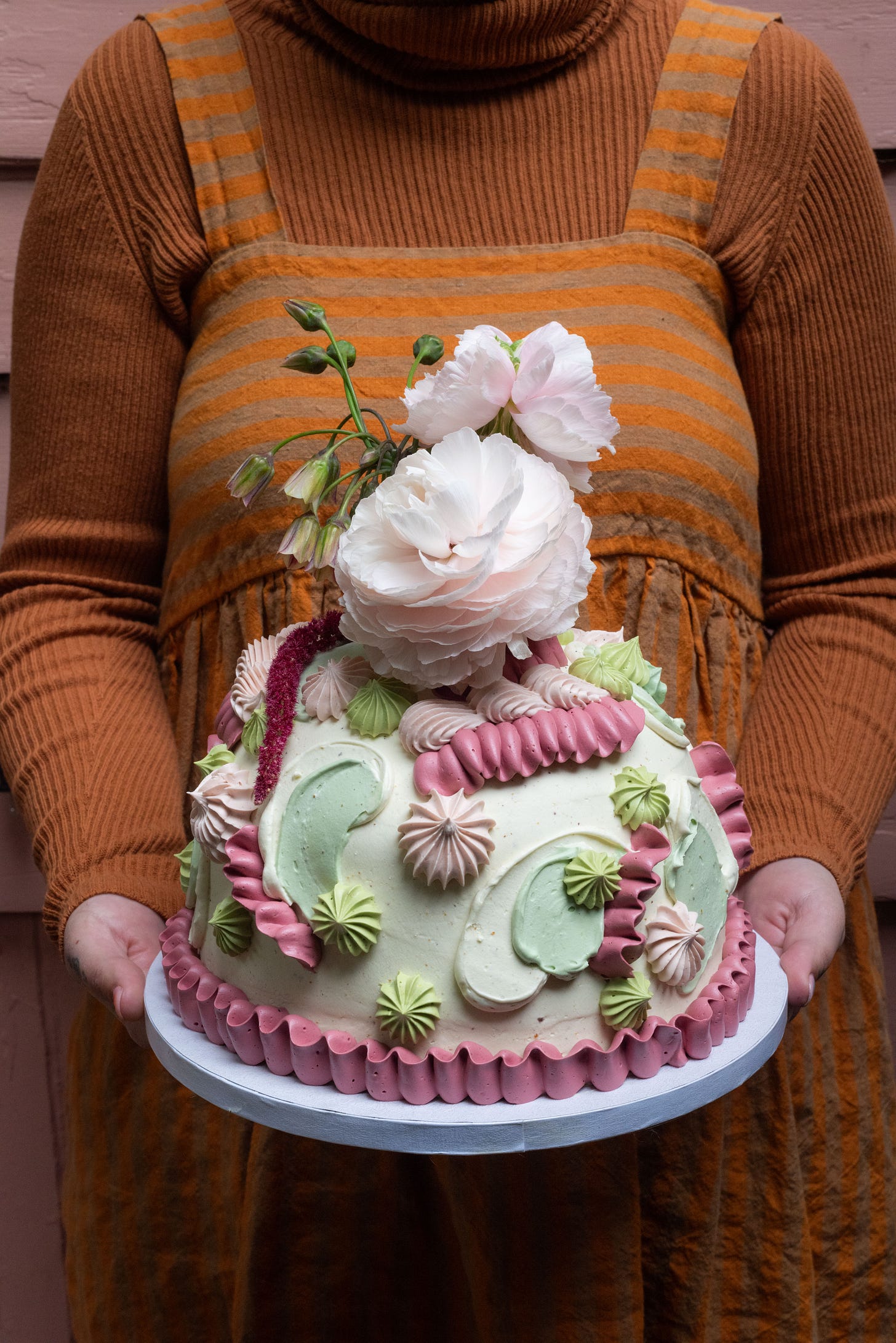 female figure in burnt orange holds a cake with flowers on top