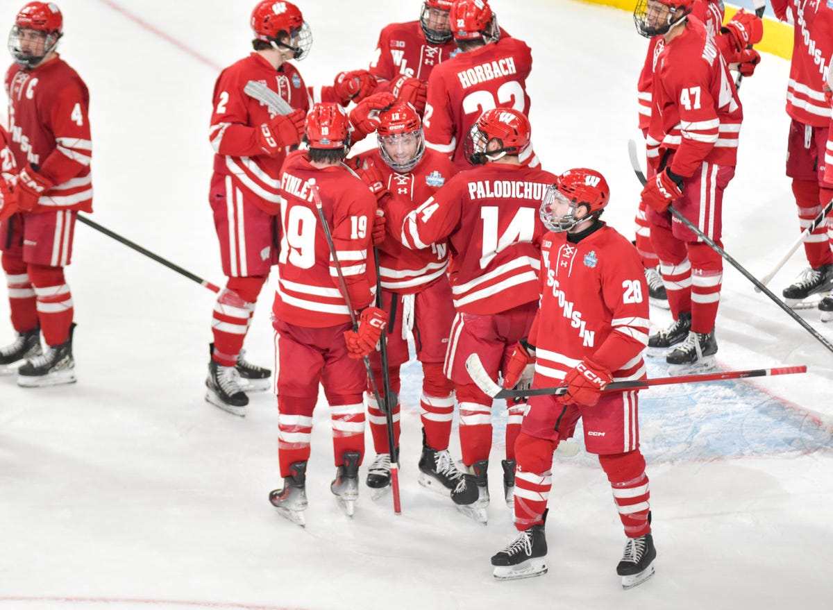 A group of Badger hockey players exchange fist bumps at the end of the ice 