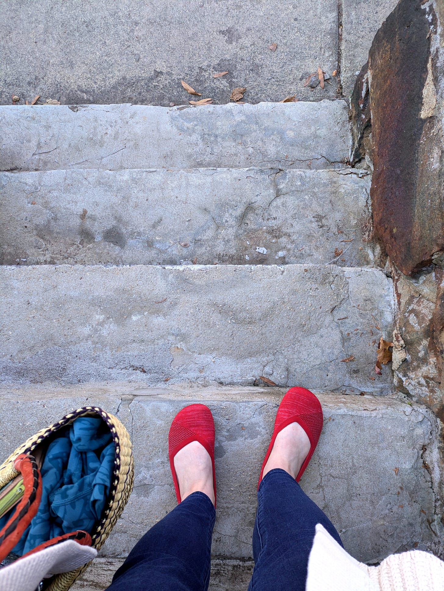 Image of woman's feet wearing red shoes and holding as basket as she stands on concrete steps.