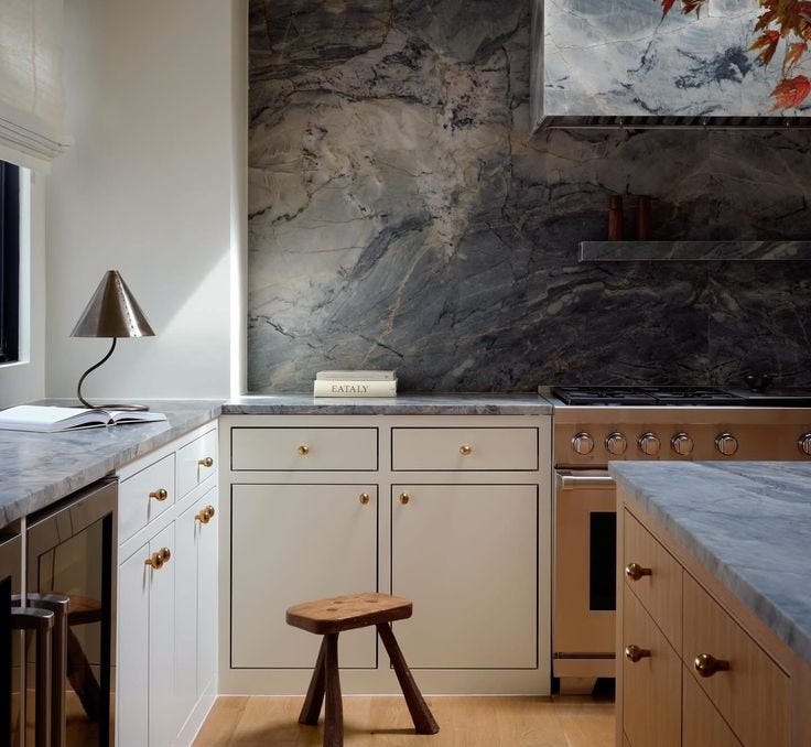 This may contain: a kitchen with marble counter tops and white cabinets, along with a wooden stool in the center