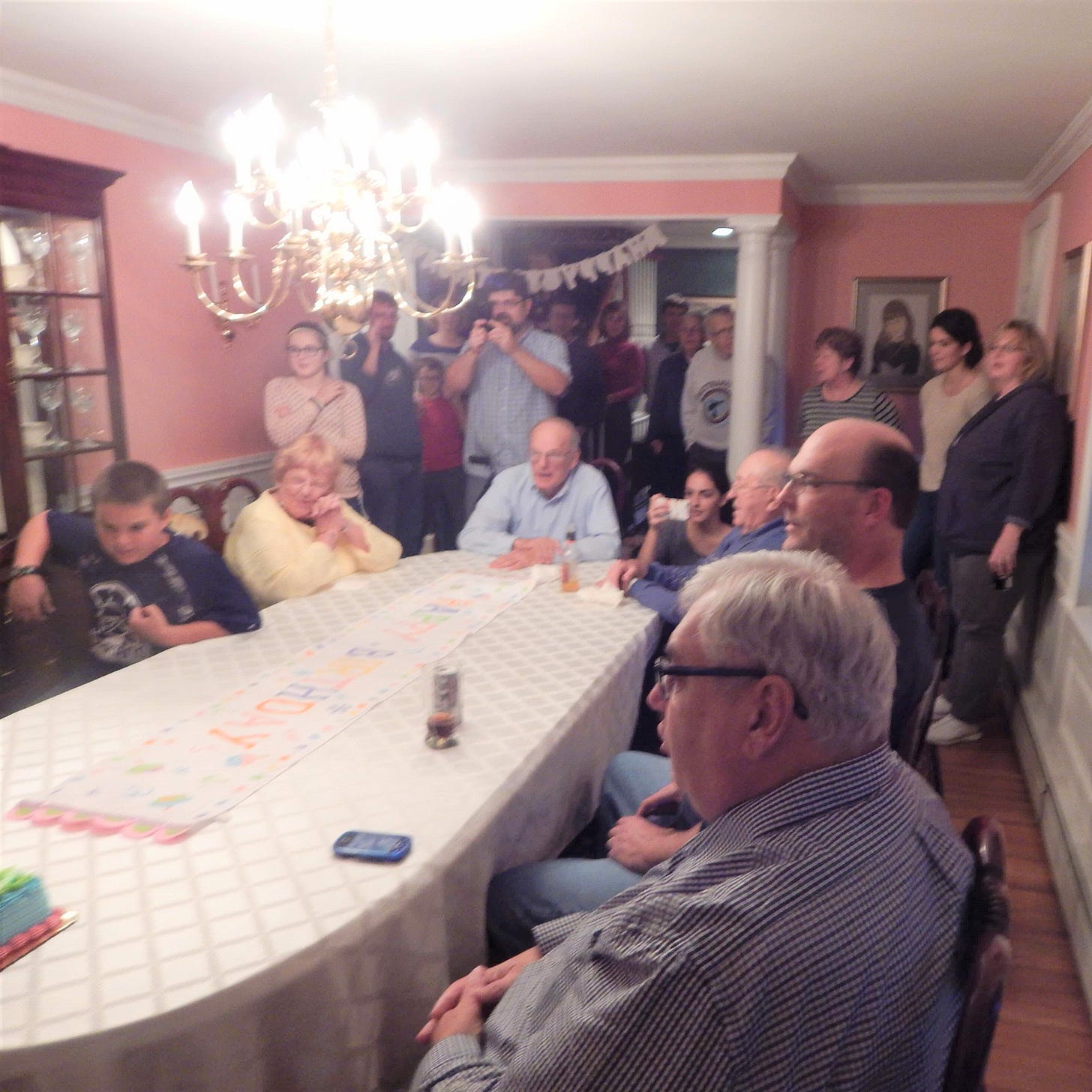 Grandparents, uncles, aunts, cousins, and siblings gathered around a dining room table looking on as the birthday child blows out the candles on their cake
