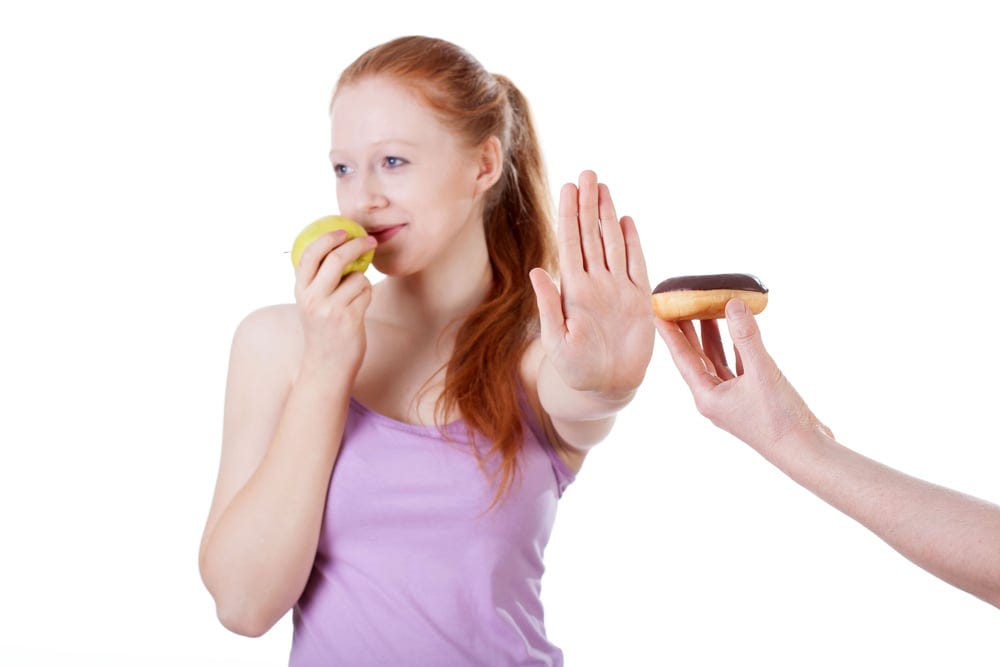 Girl with apple refusing cookie on isolated white background Girl with apple refusing cookie on isolated white background