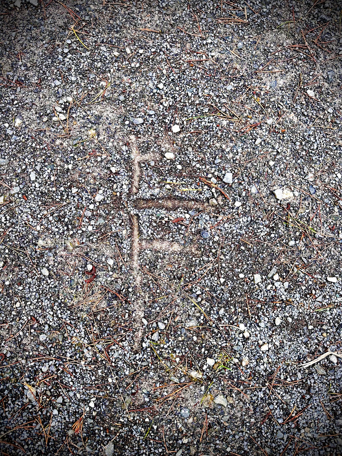 A shape is drawn on a dirt path. The shape is one longer vertical line with three shorter horizontal lines coming off the right of the vertical line