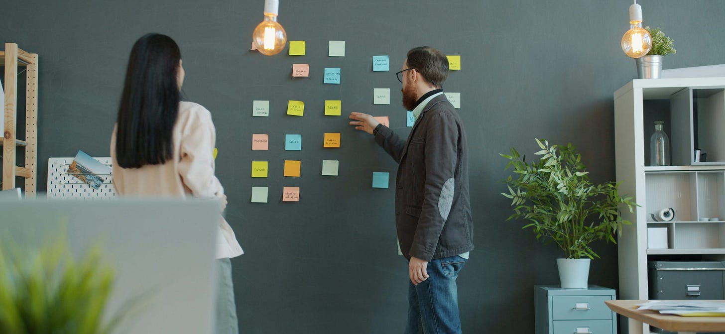 Two people planning with sticky notes on wall.