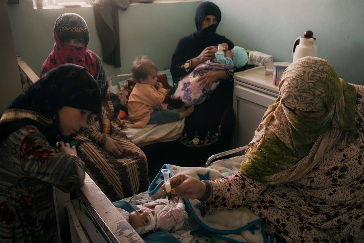 Afghan women and children receiving limited medical care in a modest setting amid humanitarian challenges