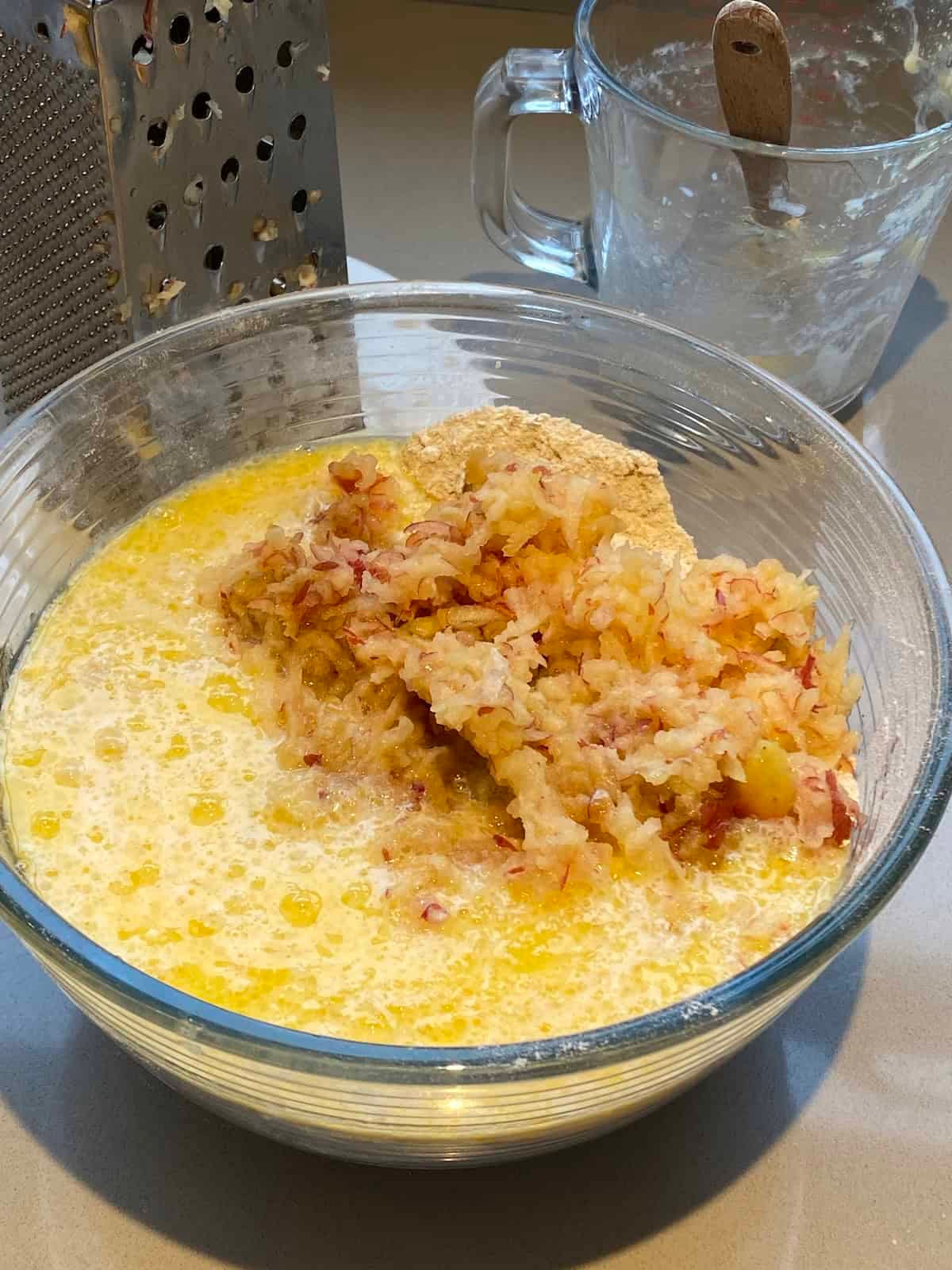 Grated apples and muffin batter in a large glass bowl. Grated apples and muffin batter in a large glass bowl.