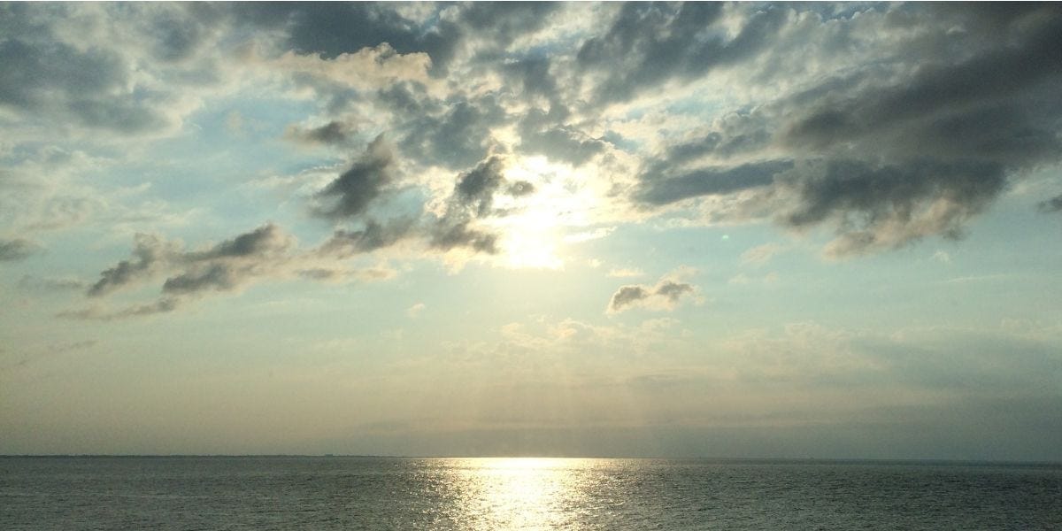 Soft sunlight breaking through clouds over calm water — photo by Dorothy Sander for the essay Above the Clouds: Finding Balance in a Noisy World.