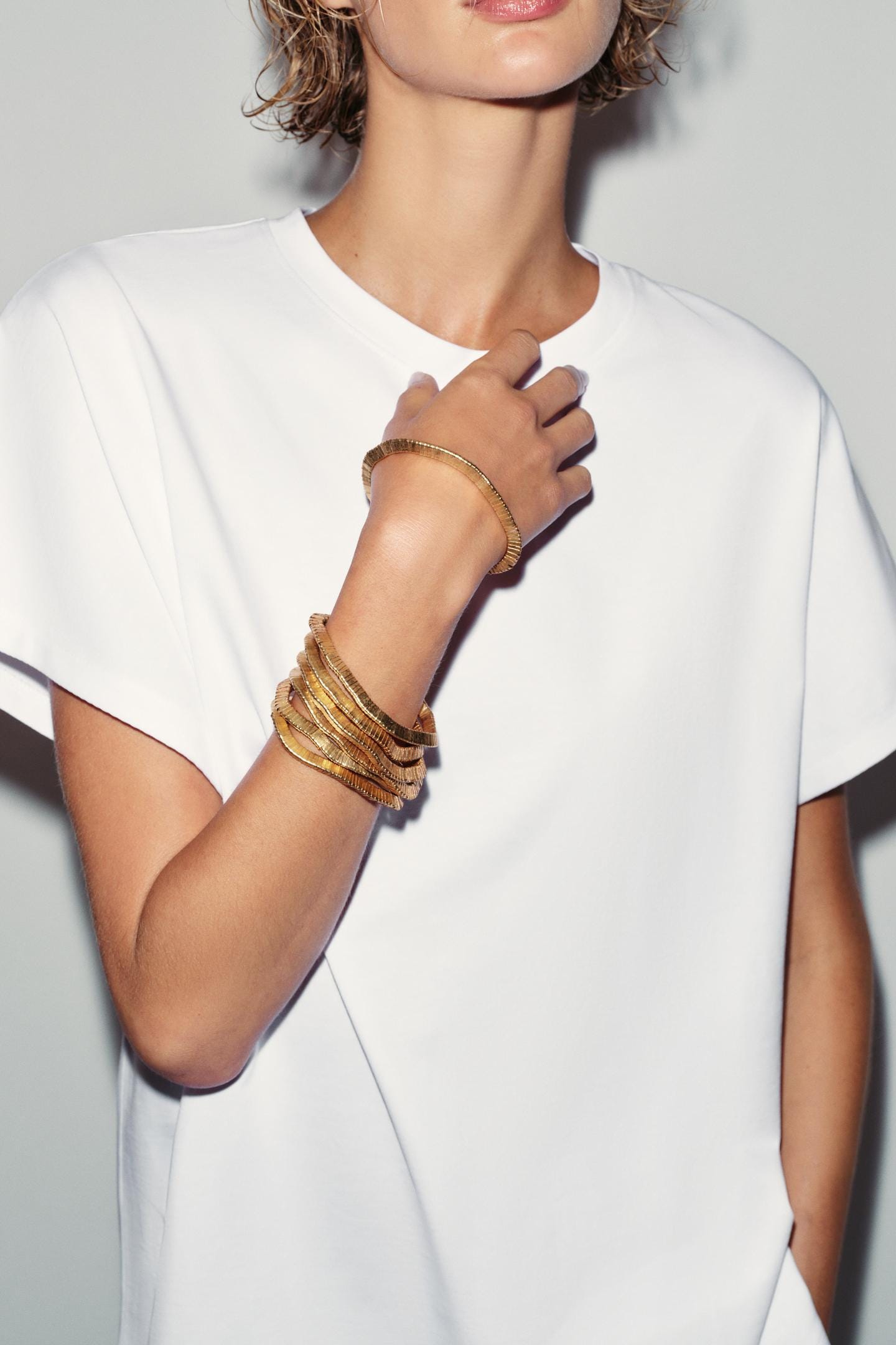 Medium shot of a white short-sleeved t-shirt and a pack of six textured gold bracelets.