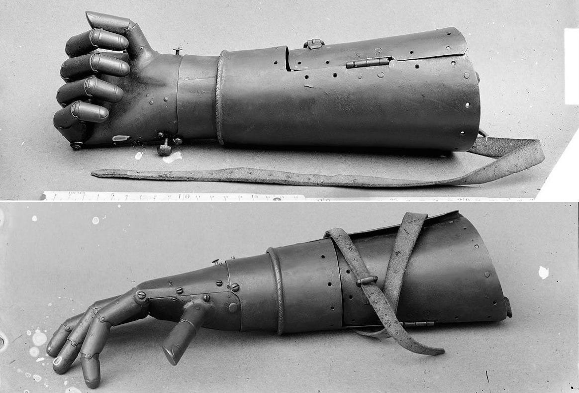 Two black and white photos of Götz’s iron hand, one showing the fingers splayed and the others showing them balled into a fist. In addition to the articulated fingers, the metal prosthetic has a cylindrical forearm segment and straps to hold the limb in place.