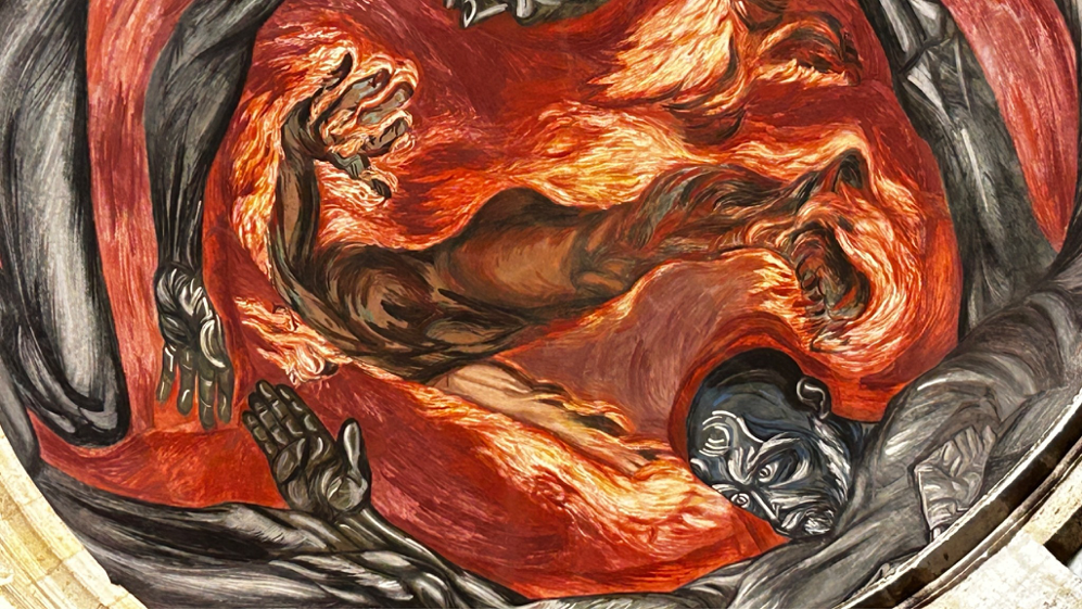 Title: Detalle de El hombre de fuego - Description: Acercamiento al mural con una figura humana rodeada por llamas naranjas y rojas.