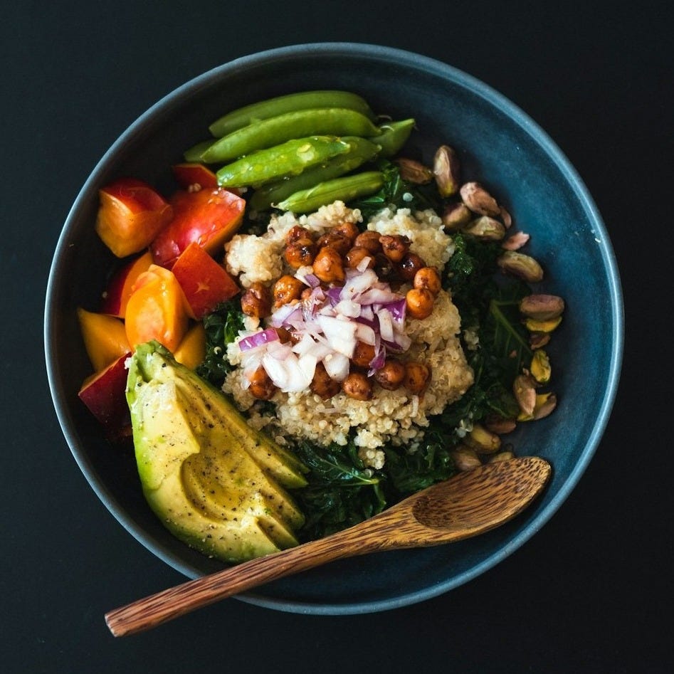a blue bowl filled with vegetables and a wooden spoon