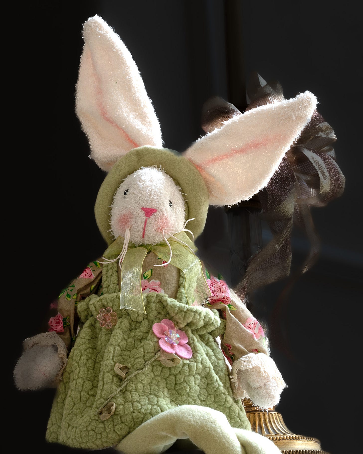 A stuffed Easter bunny sitting upright, legs-crossed, wearing a lime green bonnet, and dress with pink flowers