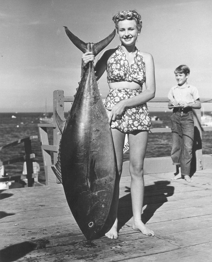 This may contain: a woman holding a large fish on a pier next to a man and boy in the background This may contain: a woman holding a large fish on a pier next to a man and boy in the background