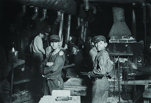A photograph shows a small group of children working in a factory. Two boys, with tattered clothes and dirt-smudged faces, stand in the forefront. A photograph shows a small group of children working in a factory. Two boys, with tattered clothes and dirt-smudged faces, stand in the forefront.
