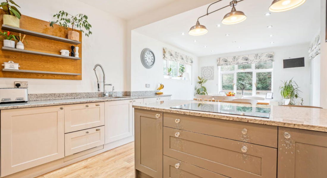 A kitchen with white and brown cabinets, shelving, a island, and lighting