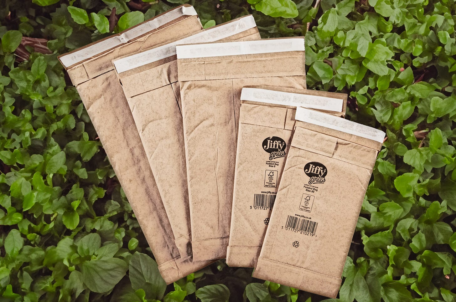 Various sizes of green jiffy bag in a garden.