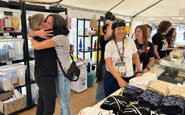 Dana Felz-Russo, left, and other volunteers selling merchandise at Tel Aviv’s Hostages Square celebrate an agreement to bring back the 48 remaining captives on October 9, 2025 (Ben Sales/Times of Israel)