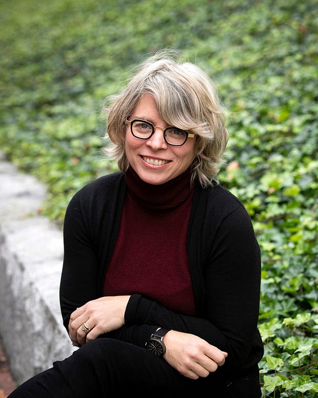 Historian Jill Lepore sitting on a stone wall in front of a grassy slope.
