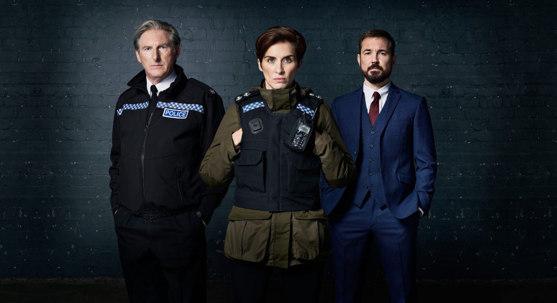Three people standing in police uniform against a black brick wall