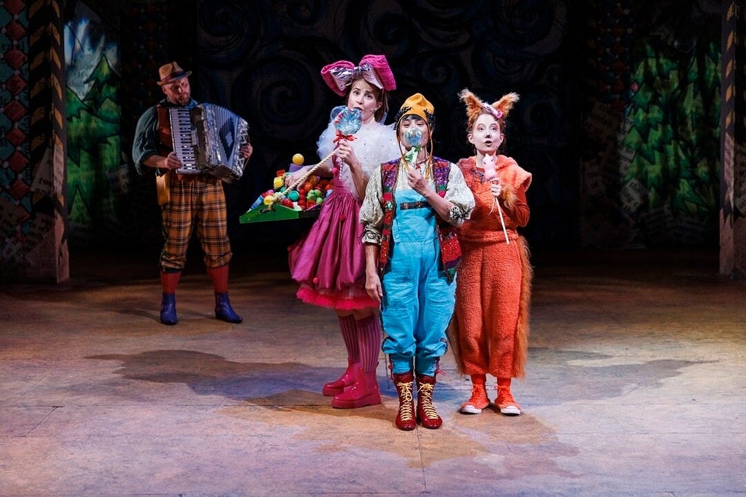 A man stands with accordian. Ih the foreground are three actors; one dressed in a pink dress, one dressed as pinocchio and one dressed as a ginger cat