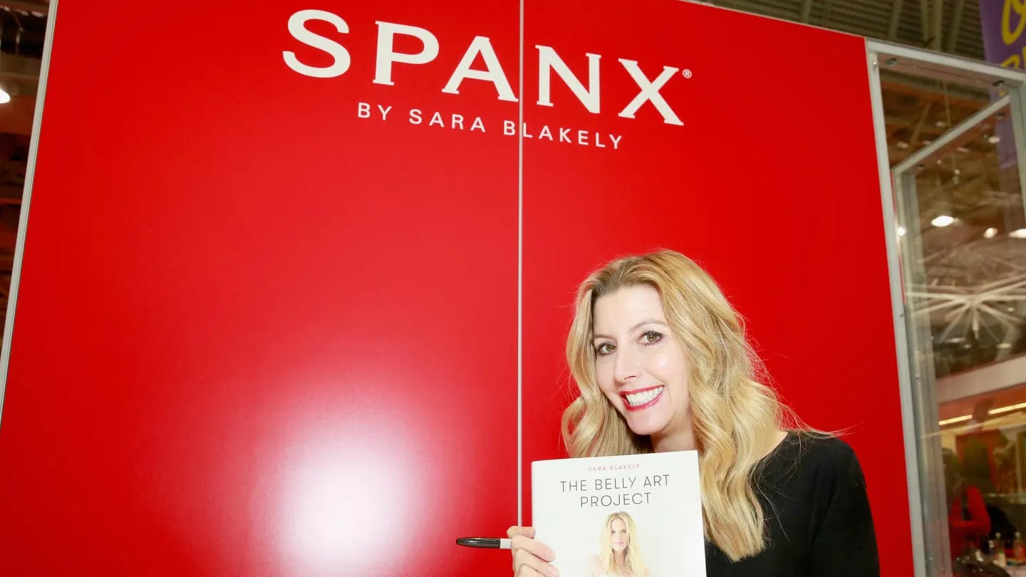 Entrepreneur holding her book in front of a red Spanx sign, symbolizing early-stage hustle and family-backed funding origins.
