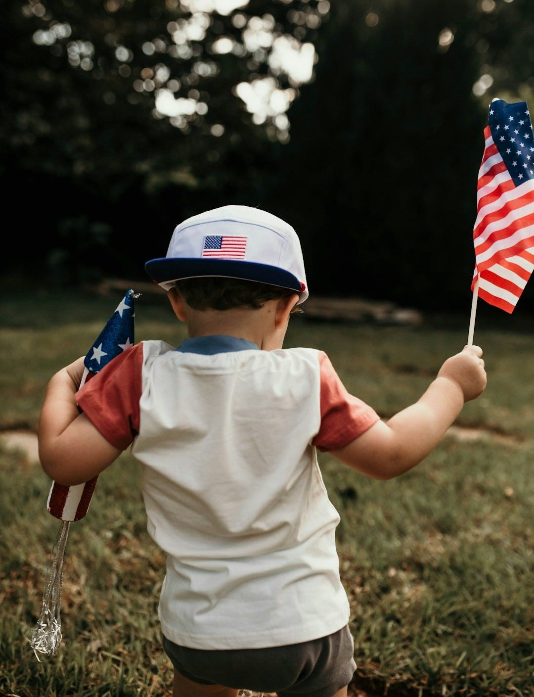 child in white crew neck t-shirt holding us a flag