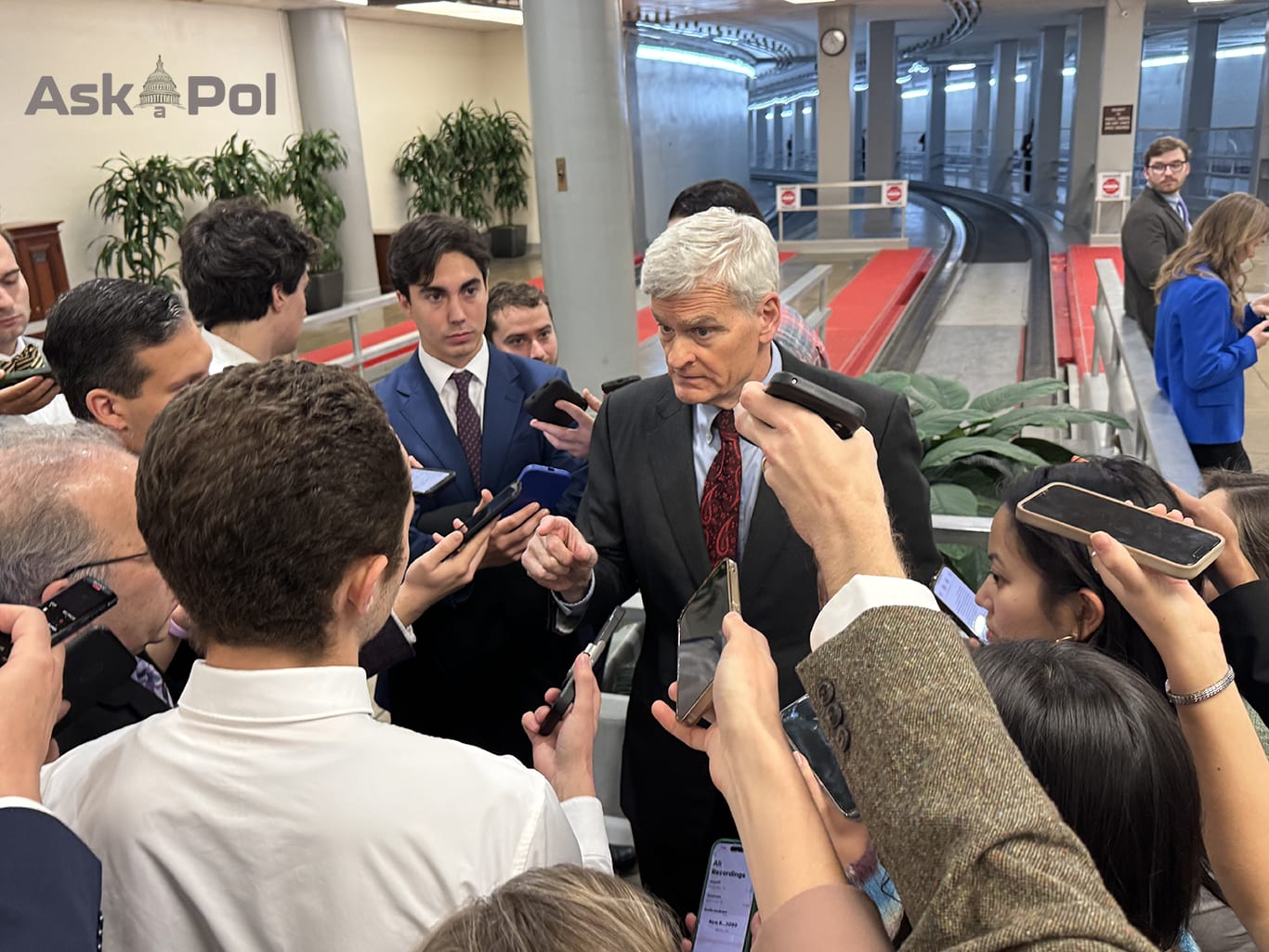 A male US Senator is surrounded by journalists and pointing at one who he's making eye contact with 
