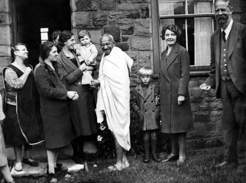 Mahatma Gandhi stands with cheering Lancashire mill workers, mostly-women.