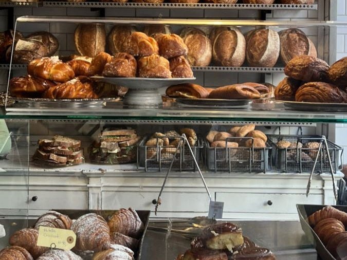 This may contain: a bakery filled with lots of different types of breads and pastries on display