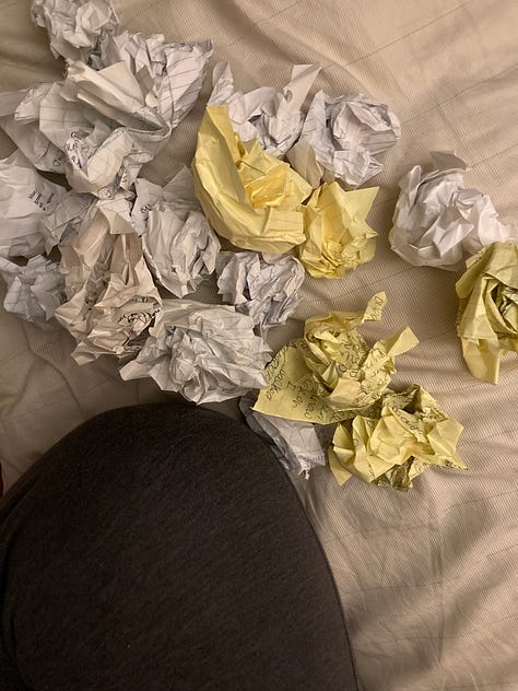 folded papers on top of jean covered notebook, crumpled paper and a knee, a small fire burning in a fire pit.
