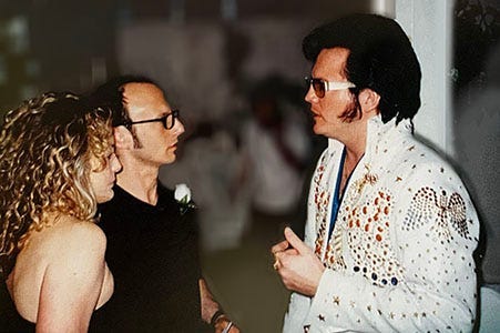 Photo of the author and a woman standing solemnly before an Elvis impersonator.