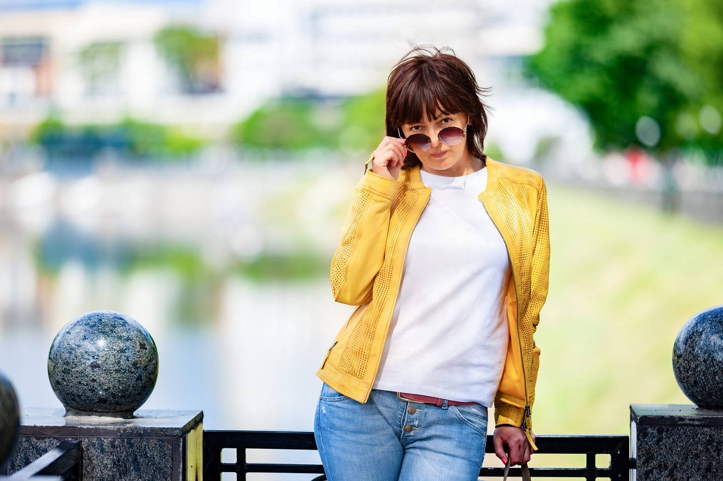 A mysterious middle-aged woman thumbs her glasses as she stares directly into the camera.