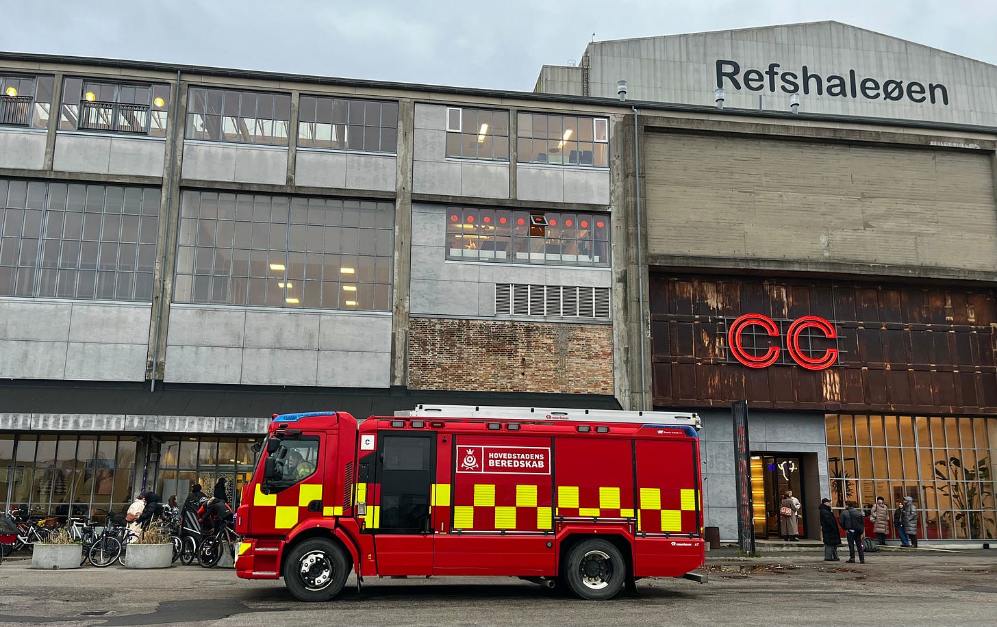 bright red fire engine outside an industrial-looking building of concrete, rust and glass
