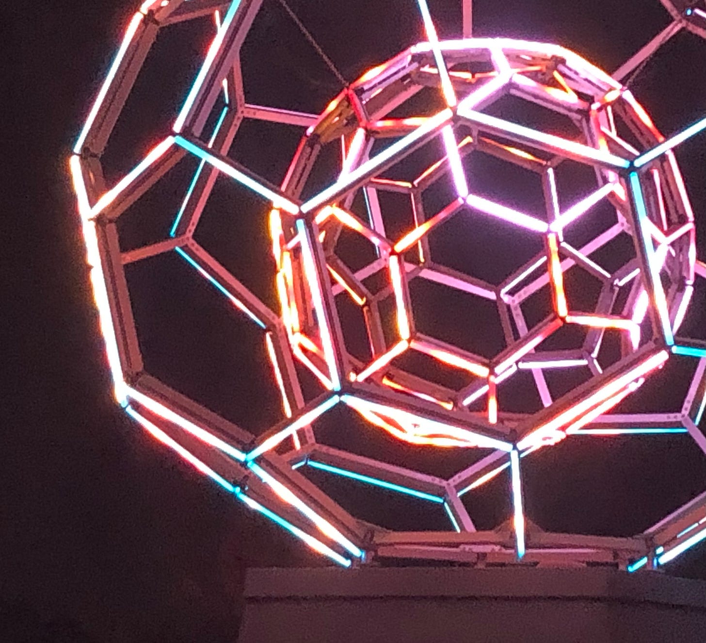 An LED soccer-ball-within-a-soccer-ball glows against the black night sky in hues of red, gold and turquoise