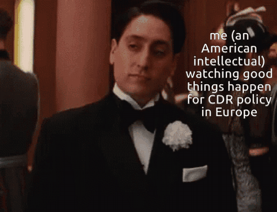 GIF of a young man in a tuxedo with a white boutonniere glancing sideways at a formal event. Text: "me (an American intellectual) watching good things happen for CDR policy in Europe"
