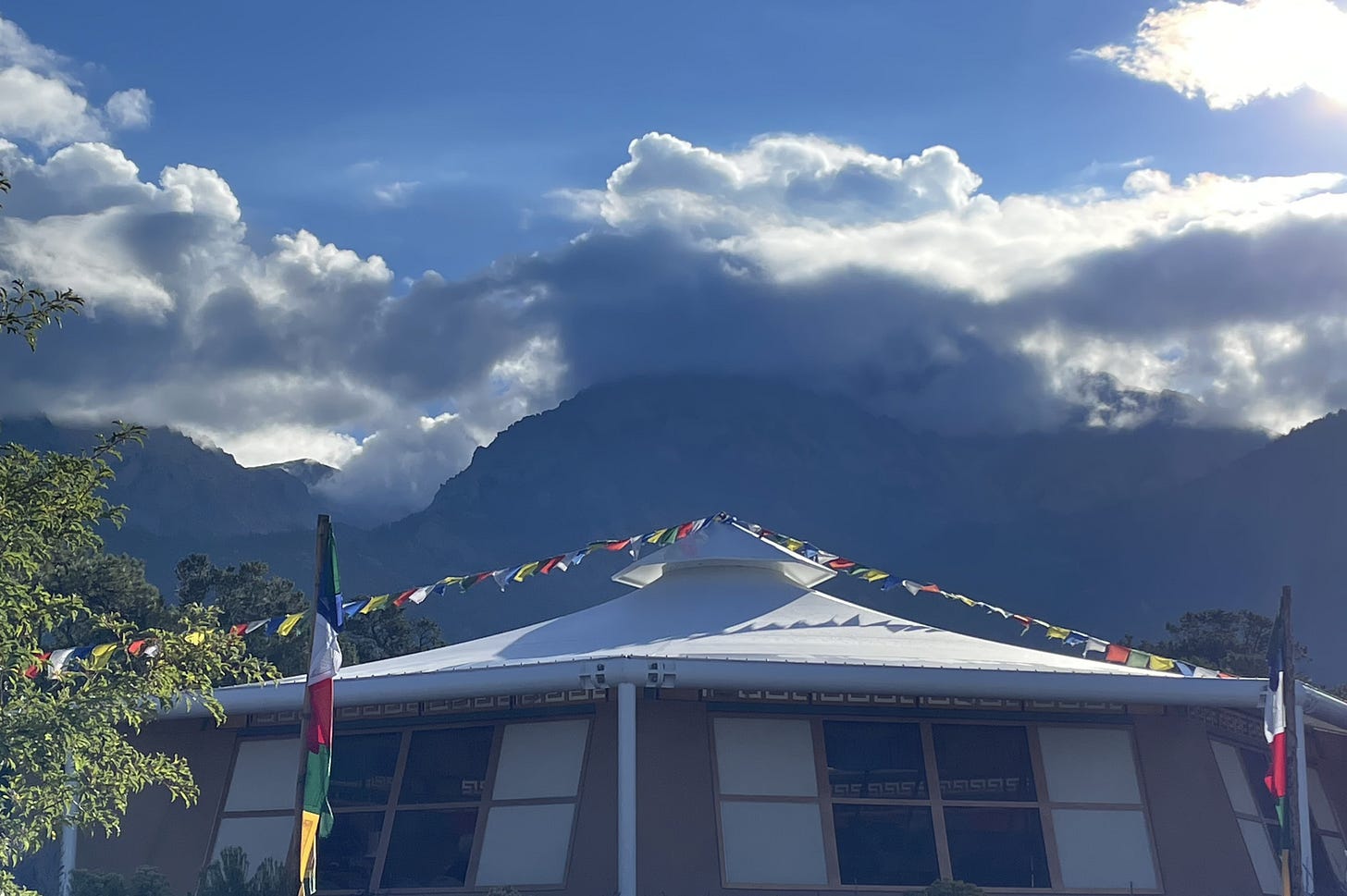 meditation hall, prayer flags, sunlit clouds over mountains