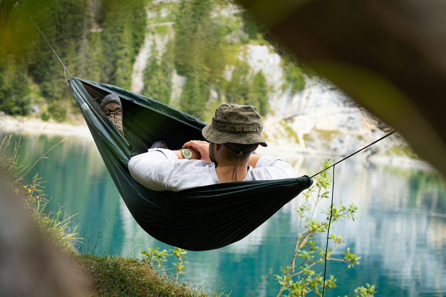 Person in hammock near lake with trees and plants surrounding the scene.