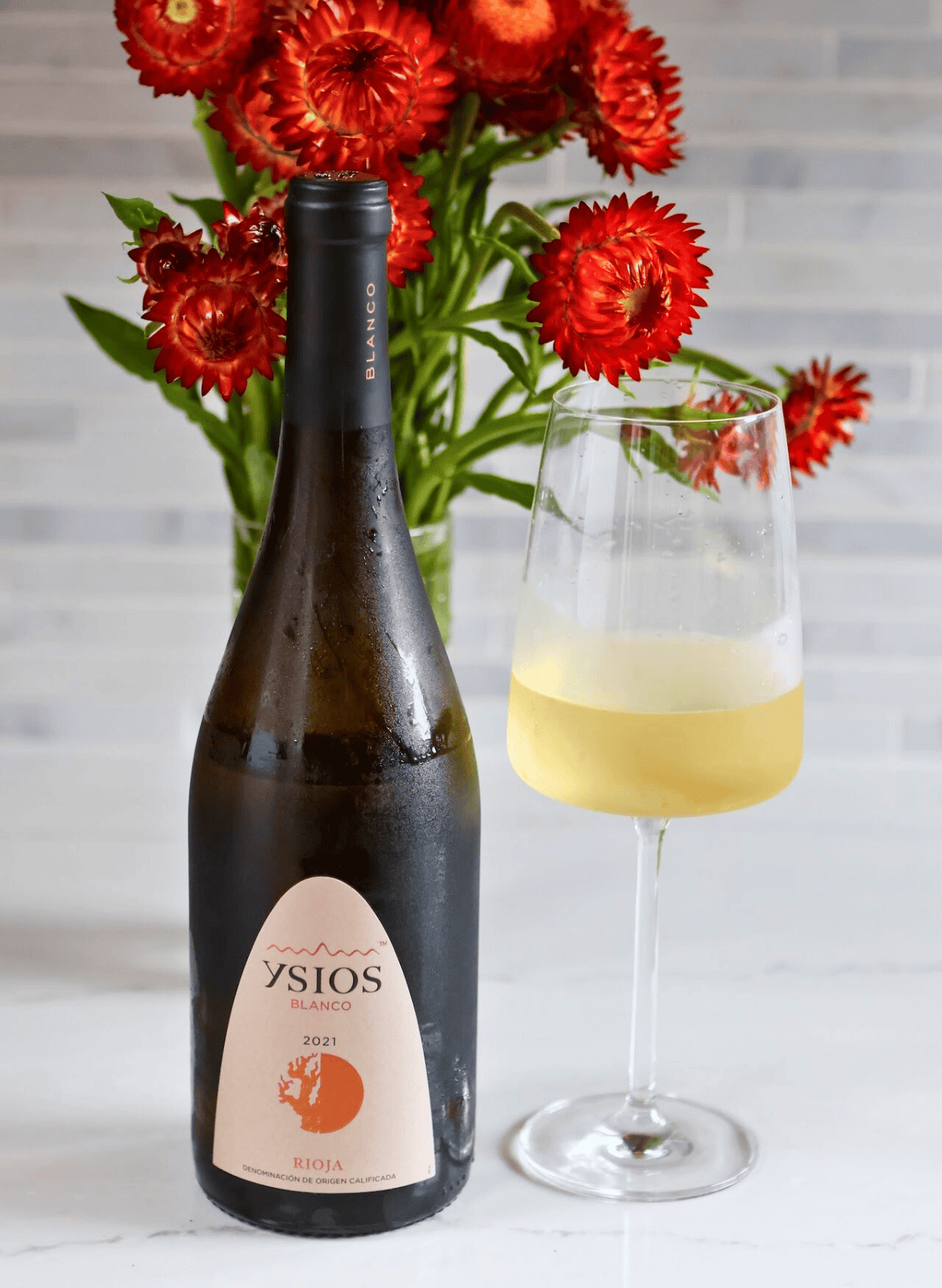 Ysios bottle and glass of white wine with red flowers in the background Ysios bottle and glass of white wine with red flowers in the background