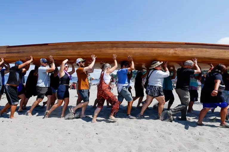 People trudge through the sand as they carry a very large strip canoe up from the water at Alki. (Jennifer Buchanan / The Seattle Times)