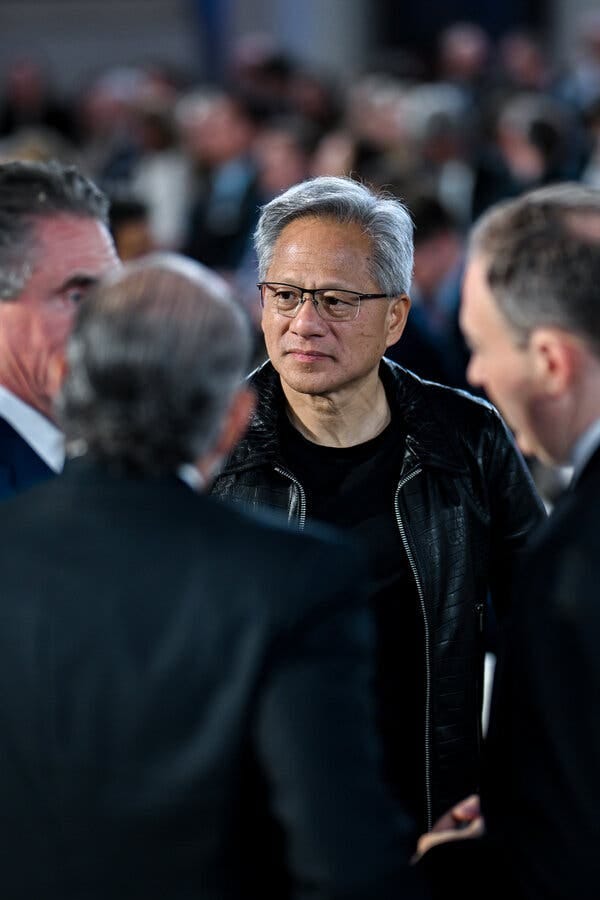 Jensen Huang, in a black jacket and shirt, speaks to three other men.