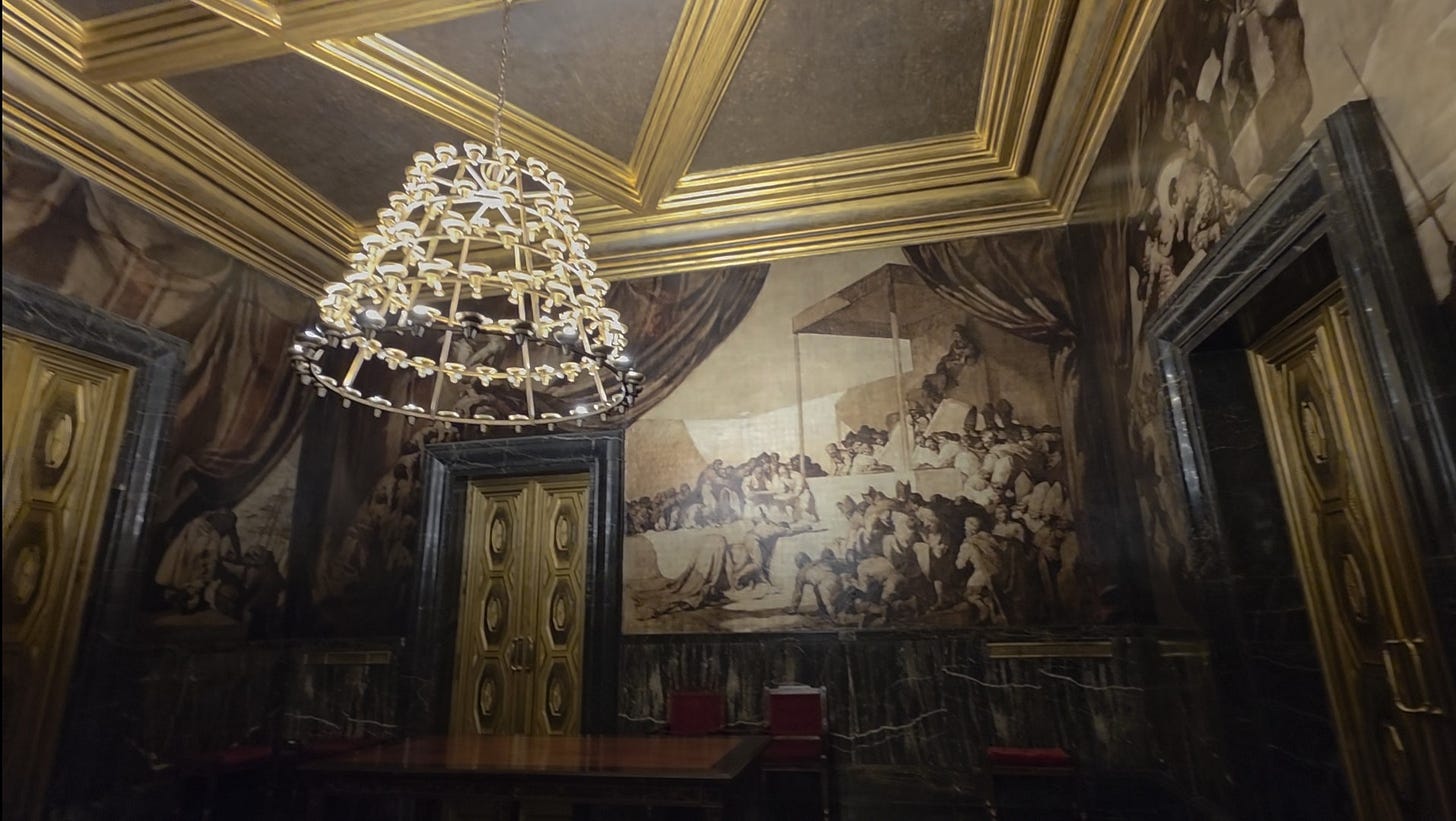 Interior del saló de Cròniques en el Ayuntamiento de Barcelona. Se aprecia una gran lámpara de araña dorada colgando de un techo artesonado con relieves de oro. Las paredes con enormes pinturas de Josep María Sert.